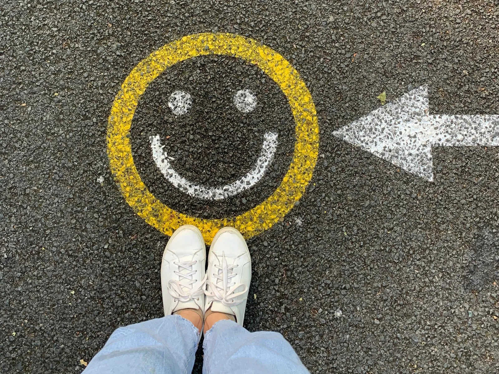 Looking down at your own feet beside a smiley face painted on the tarmac
