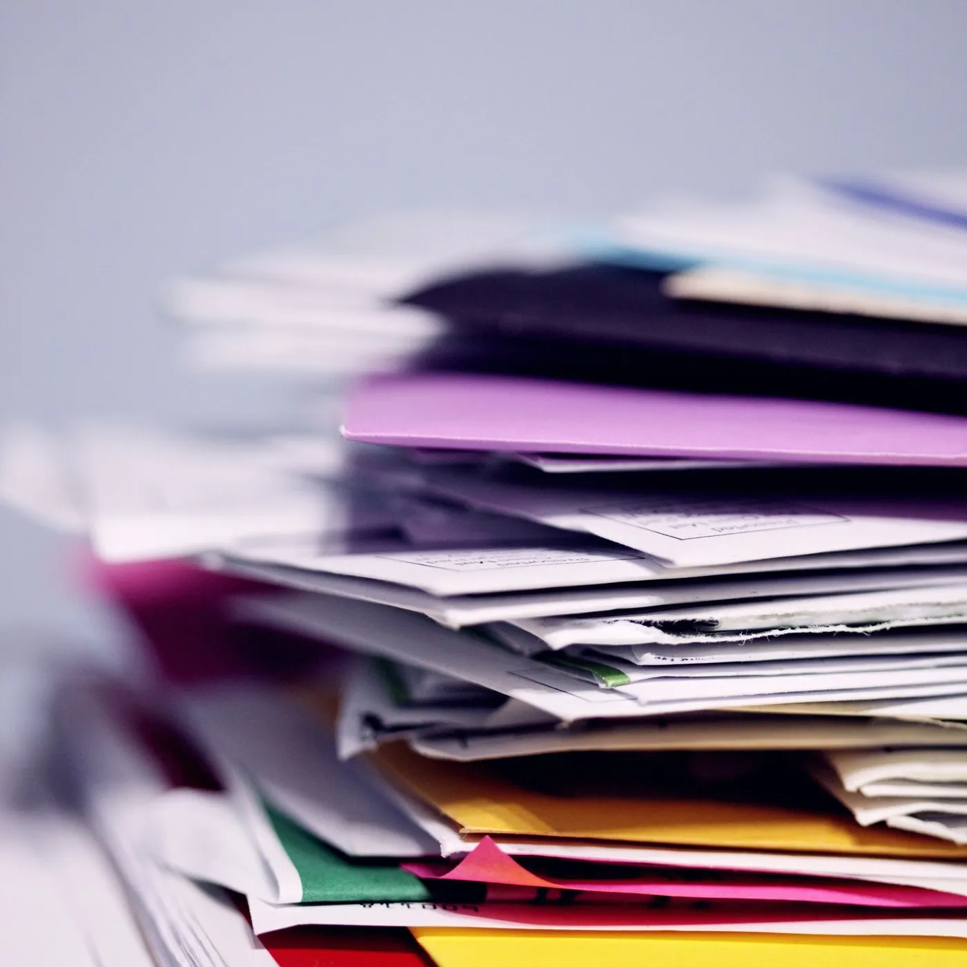 A tall stack of paper reports and folders in mixed colours